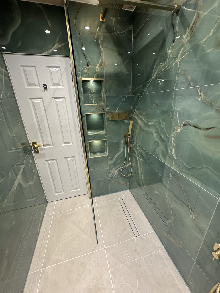 Completed walk-in shower with green marble-effect tiles and brass fittings